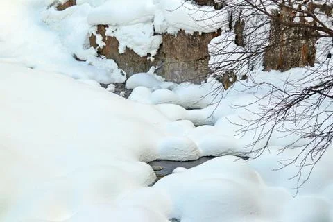 Mountain stream flows among the rocks and puffy white snow on the banks Stock Photos