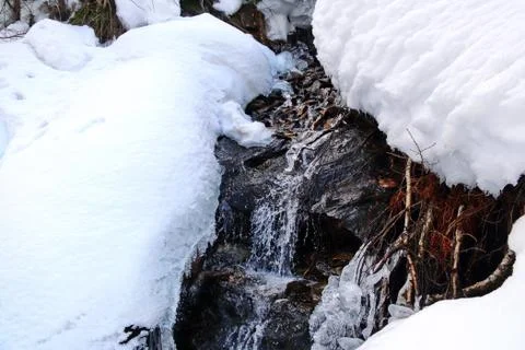 Mountain stream flows among the rocks and puffy white snow on the banks Stock Photos