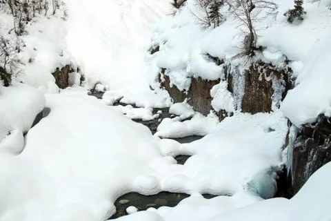 Mountain stream flows among the rocks and puffy white snow on the banks Stock Photos