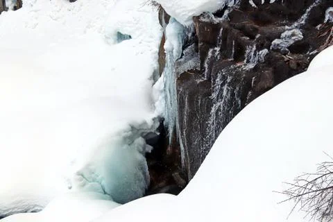 Mountain stream flows among the rocks and puffy white snow on the banks Stock Photos