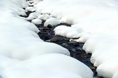 Mountain stream flows among the rocks and puffy white snow on the banks Stock Photos