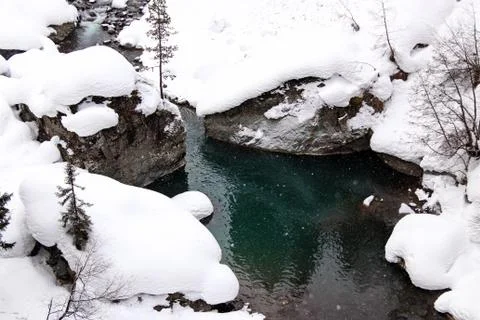 Mountain stream flows among the rocks and puffy white snow on the banks Stock Photos