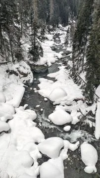 Mountain stream flows among the rocks and puffy white snow on the banks Stock Photos