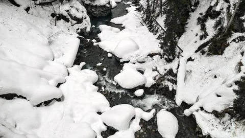 Mountain stream flows among the rocks and puffy white snow on the banks Stock Photos