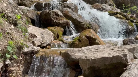Mountain stream flows between large rocks with fresh water moving through a natu Stock Footage 341408295