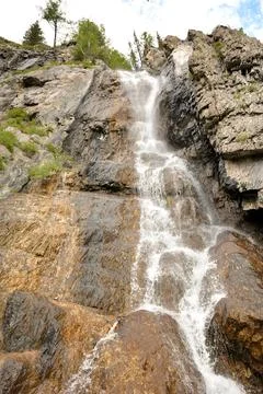 A mountain stream flows down a high cliff in a cascading waterfall on a clo.. Stock Photos