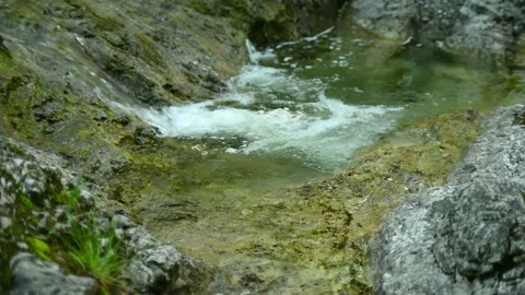 A mountain stream flows over rocks into a small pool Video stock 211470064