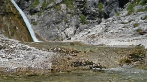 A mountain stream flows over rocks in front of a waterfall (slow motion) Stock-Footage 219636707
