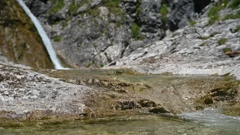 A mountain stream flows over rocks in front of a waterfall (slow motion) Stock-Footage 219636728