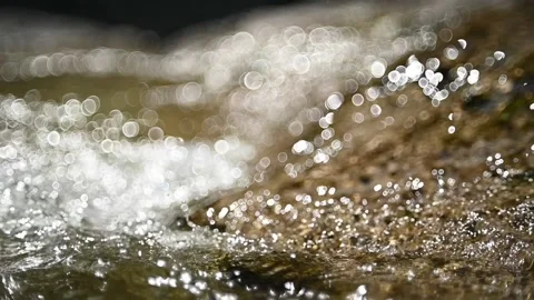 A mountain stream flows over rocks in the sunlight (slow motion, bubble bokeh) Video stock 219640315