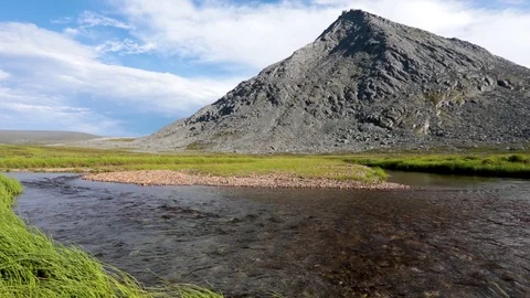 A mountain stream flows through the valley against the backdrop of the mountains Видео 93953121
