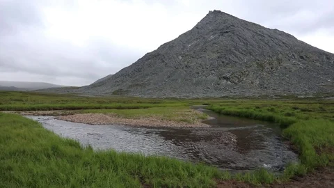 A mountain stream flows through the valley against the backdrop of the mountains Stock Footage 93954221