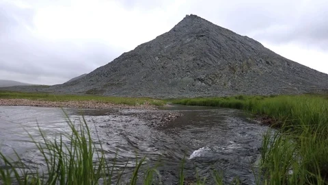A mountain stream flows through the valley against the backdrop of the mountains Видео 93954261