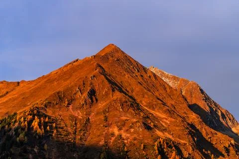 Mountain summit dramatic red stone in sun light with snow cover, copy space Stock Photos