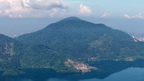 Mountain with a tall tower on top and a lake below at Mengkuang Dam Stock Footage 332214054