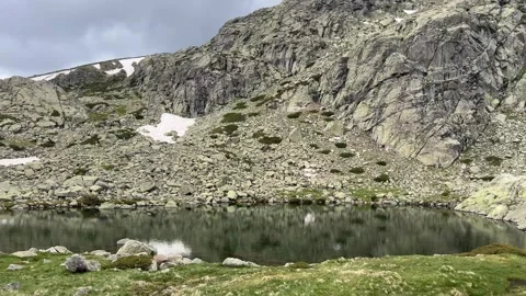 Mountain Tarn Reflecting Rocky Slope and Late Spring Snow Patches Stock Footage 337944038