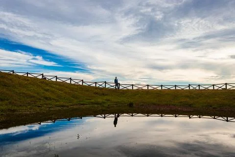 Mountain top lake view with dramatic sky and isolated girl with water reflect Foto stock