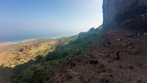 Mountain trail by steep cliff overlooking turquoise sea Stock Photos