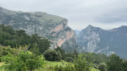 Mountain valley landscape with dramatic cliffs and cloudy sky, slow right pan,4K Stock Footage 333903383