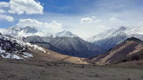 Mountain valley stretches between snowy peaks with rocky slopes and clouds above Stock Footage 340890346