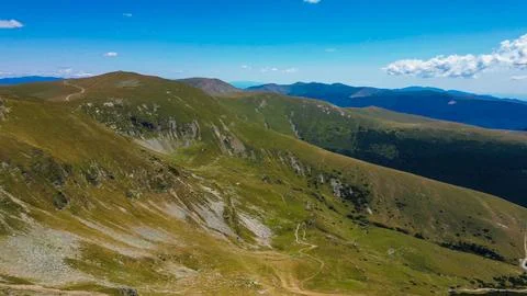 Mountain valley with winding path and rocky slopes under clear sky Stock Photos
