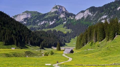 Mountain view with a path and small buildings under a clear sky in a green Stock Photos