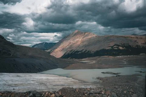 Mountain View: Rugged Peaks, Cloudy Skies, and Glacial Waterscape below. Stock Photos