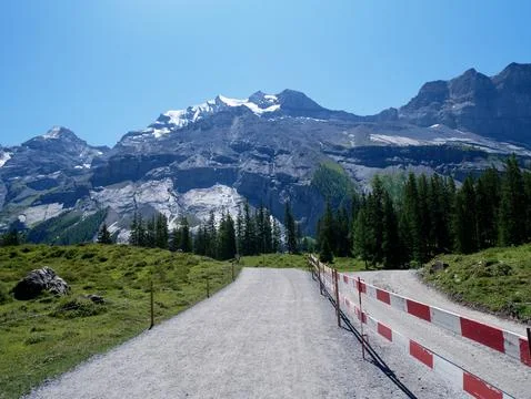 Mountain walking trail bordered by safety caution tape under alpine peaks Foto stock