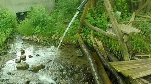 Mountain water spring flowing from rubber hose on wooden construction Stock Footage 314979292