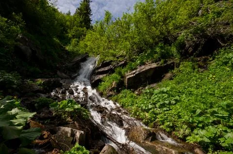 Mountain waterfall on the background of the sky with a summer sunny day. Stock Photos