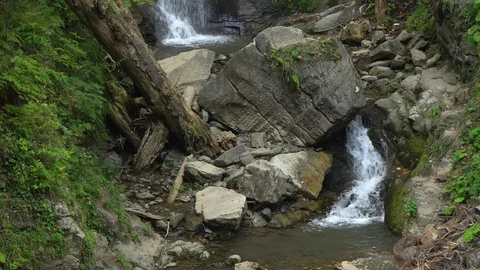 Mountain waterfall creates stream under fallen brown rock Stock Footage 116873130