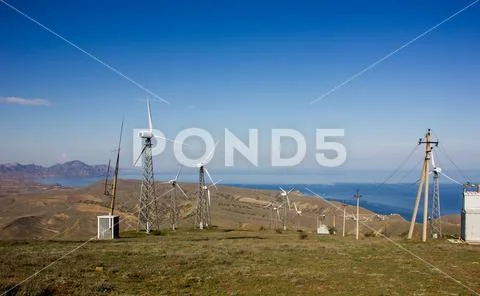 Mountain wind turbines against the backdrop of mountains and the sea. Stock Photos