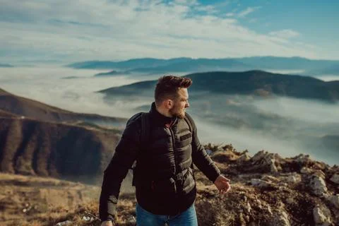 A mountaineer in a jacket and with a backpack standing on top of the mountain Foto stock