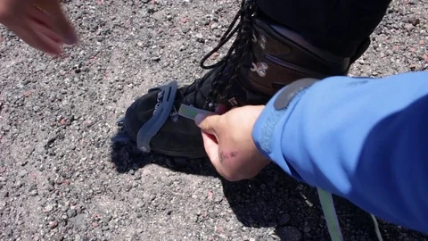 Mountaineer man is dressing on and spanning crampons on his boots using belt. Stock Footage