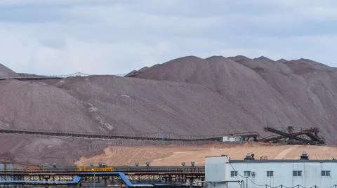 Mountains of empty ore when mining potassium on cloudy sky background. Transp Stock Photos