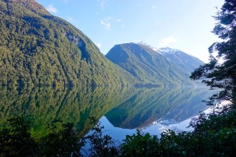 Mountains partially snow capped reflect in a lake with Forrest as a framing Foto stock