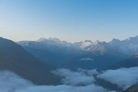 Mountains pierce through soft clouds in an alpine morning spectacle now. Stock Photos