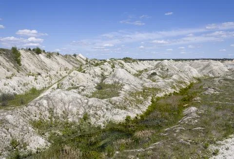 Mountains of processed chalk ore overgrown with green young plants on the bac Stock Photos