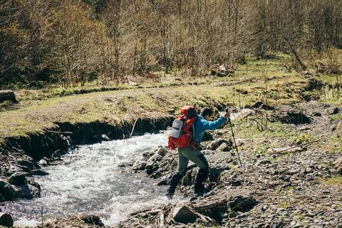 Mountains, river, man with a backpack crosses the river Stock Photos