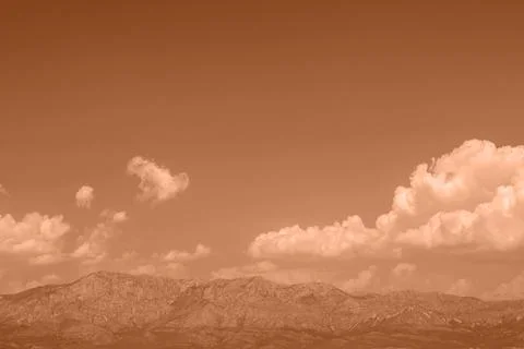 Mountains stand under a cloudy sky at dusk with a warm orange tint during t.. Stock Photos