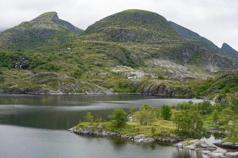 Mountains surrounded lake with waterfall far away cloudy weather Stock Photos