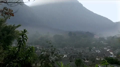 Mountains tower over a small Dai village in China’s Yunnan Province.  Stock Footage 158822203