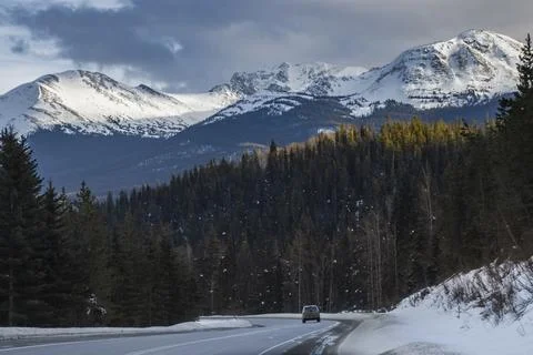 Mountains tower over winding road with car driving during winter afternoon .. Stock Photos