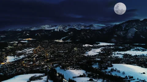 Mountains at winter night, aerial view. Illuminated city covered with snow Stock Footage