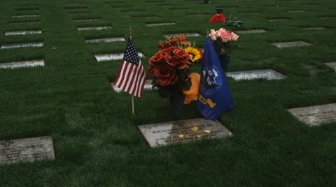 A mourner kneels and brushes away leaves from a veteran's gravestone Stock Footage 59189961