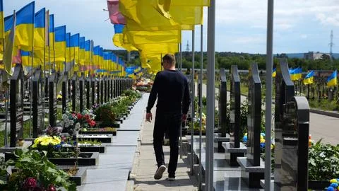 Mourning man go among countless graves of ukrainian soldiers with national fl Stock Photos