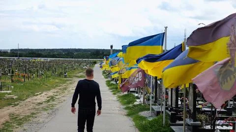 Mourning man go among countless graves of ukrainian soldiers with national fl Stock Photos