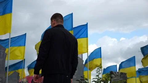 Mourning man standing among countless graves of ukrainian soldiers with natio Stock Photos