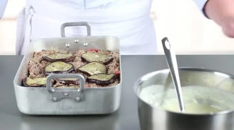 Moussaka being made: Bechamel sauce being poured over minced meat and aubergines Stock Footage 24671249