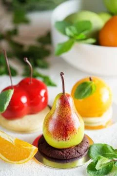 Mousse dessert in the shape of a pear fruit, orange fruit and cherry. Stock Photos